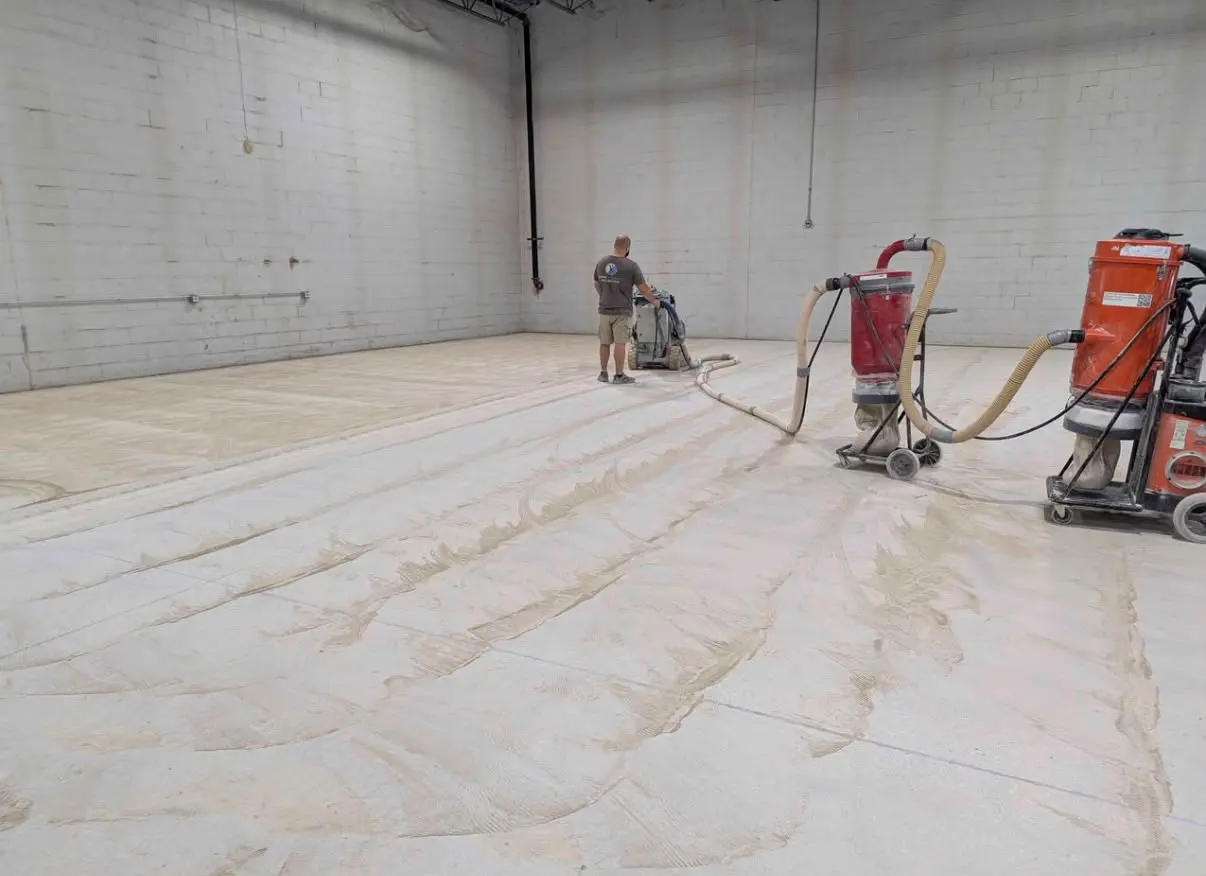 Crew member running a floor grinder with dust extractors in an empty concrete room