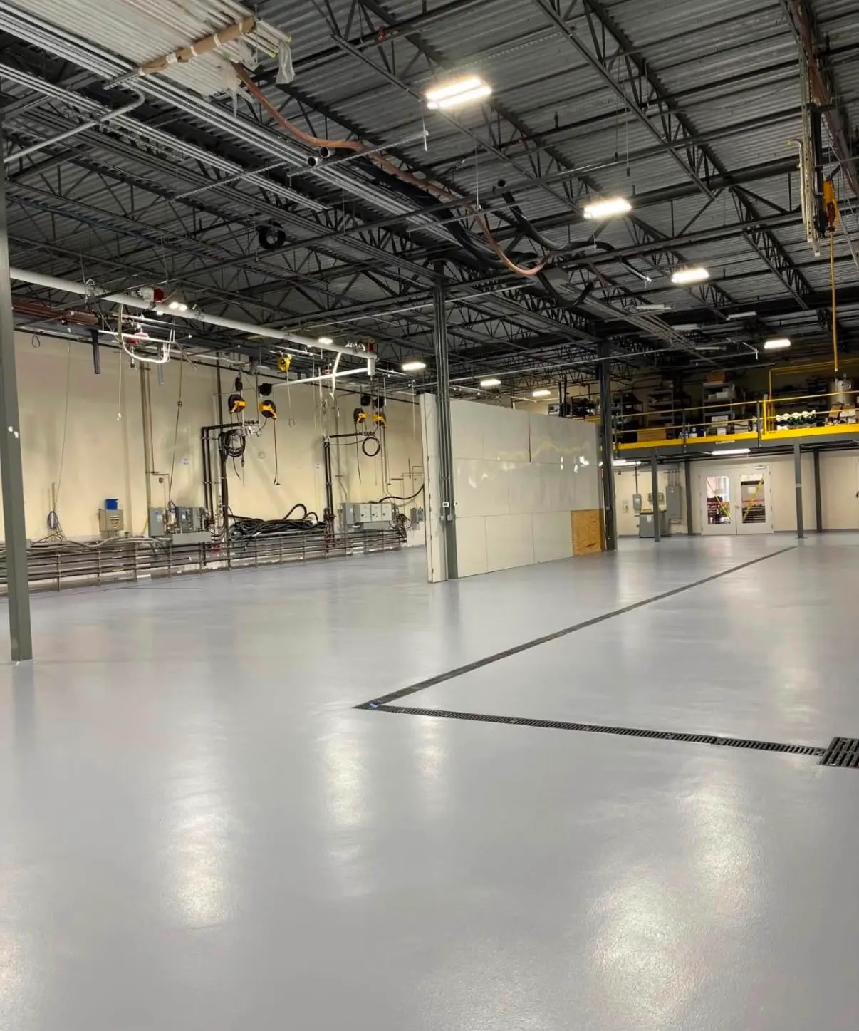 Light gray coated shop floor with trench drains and a mezzanine behind