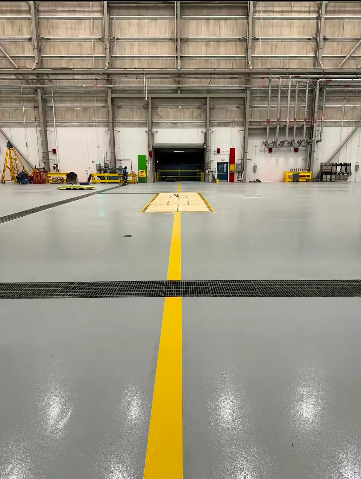 Yellow line crossing a trench drain toward the back wall of the hangar