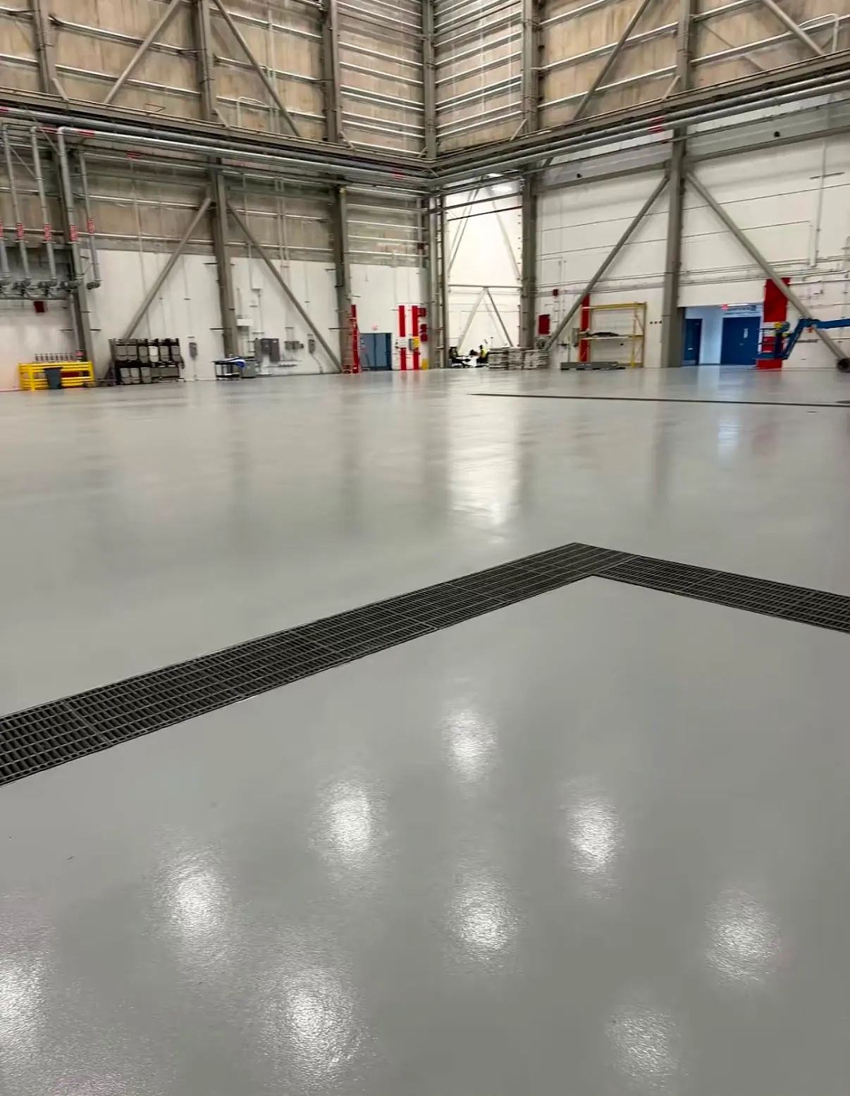 Trench drains meeting at an angle in a glossy gray hangar floor